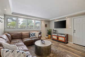 Recessed lighting illuminates this living space featuring a row of four windows with white plantation shutters, wood-finish flooring, and crown molding