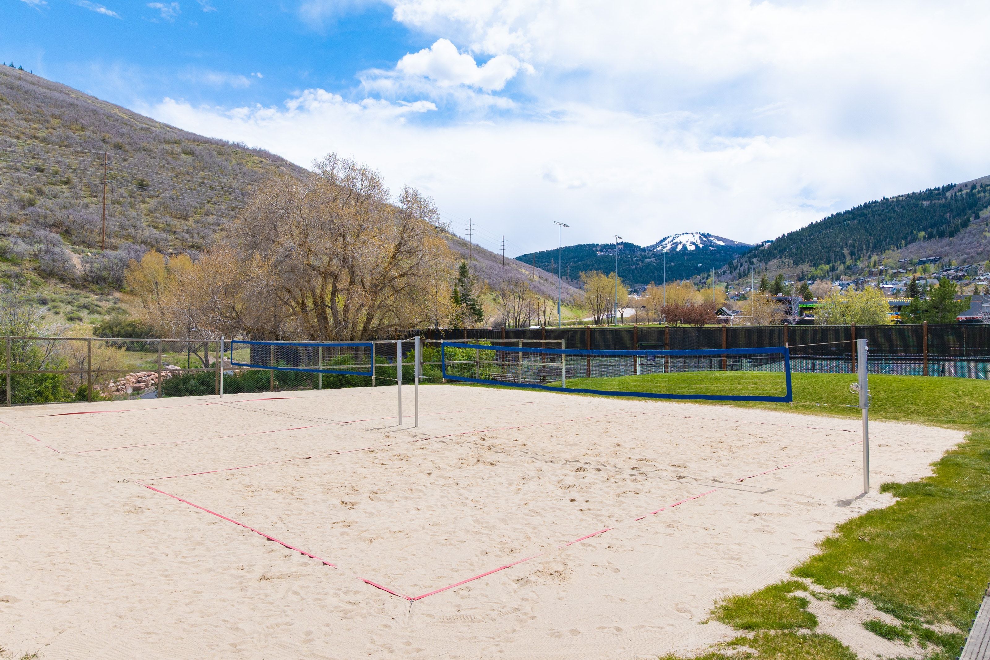 Sand volleyball court featuring a net and boundary lines, bordered by green grass