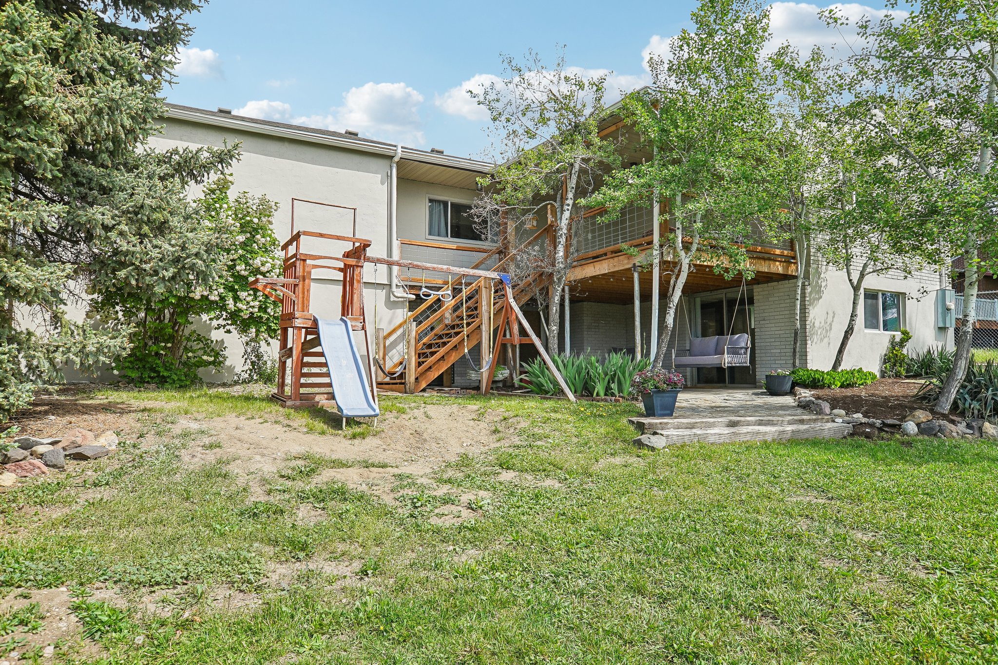 Expansive rear exterior featuring a multi-level wood deck with stairs, a ground-level patio, and mature trees providing natural screening