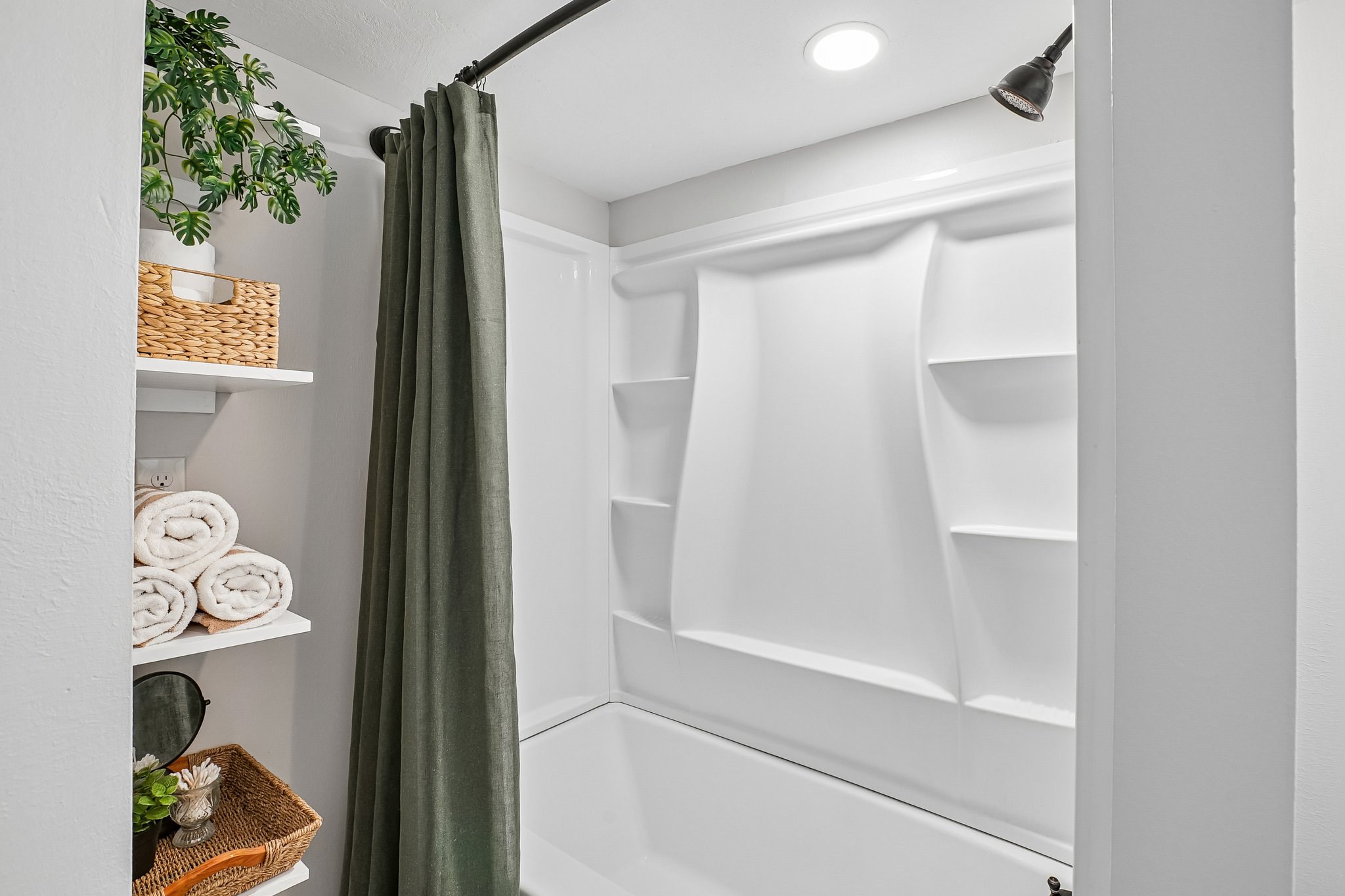 White bathtub and shower surround with integrated shelving, matte black shower head, recessed lighting, and built-in shelving