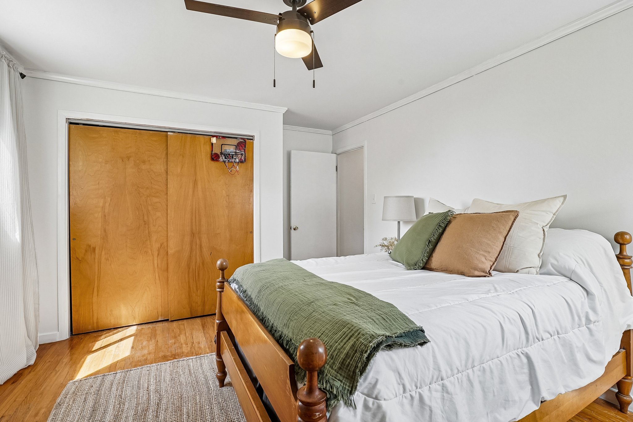 Bright bedroom featuring wood-finish flooring, white walls, and a ceiling fan with integrated lighting