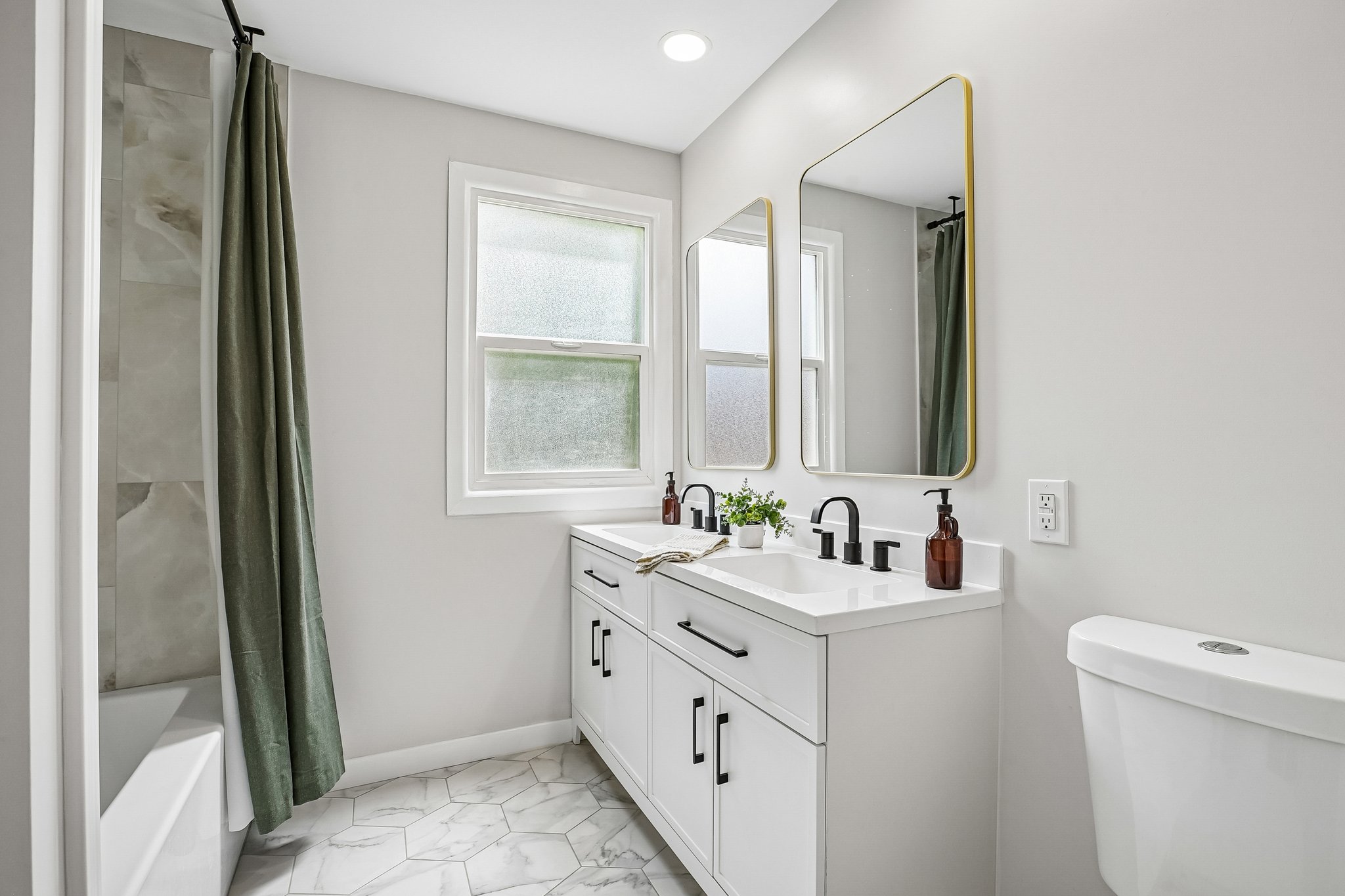 Dual vanity featuring white cabinetry, black hardware, and two gold-framed mirrors