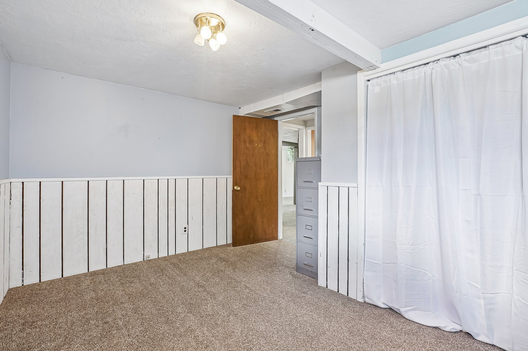 Carpeted interior space featuring white vertical panel wainscoting and light blue wall paint