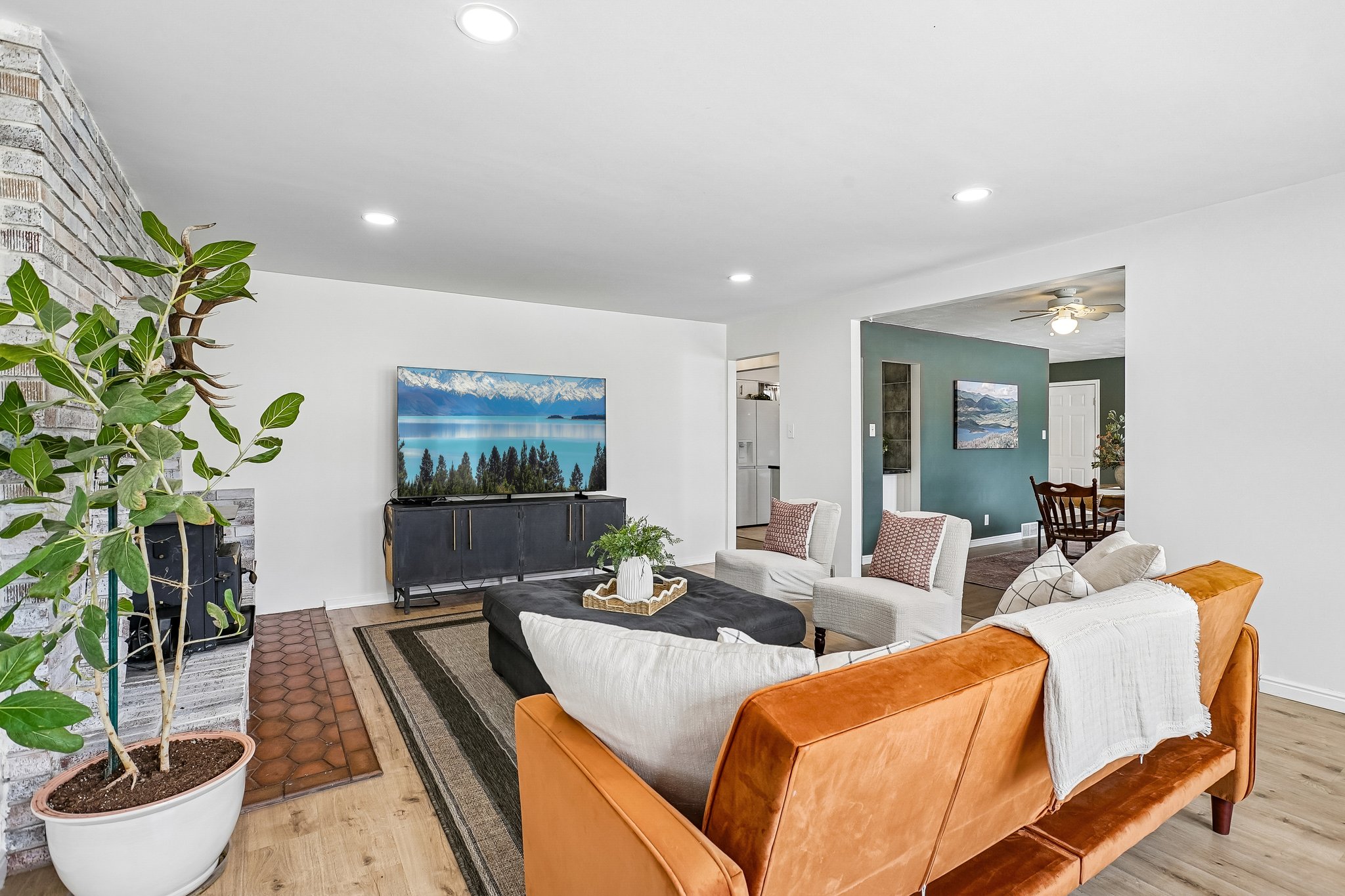 Spacious living area featuring light wood-finish flooring, recessed lighting, and a white brick fireplace with a terracotta tile hearth