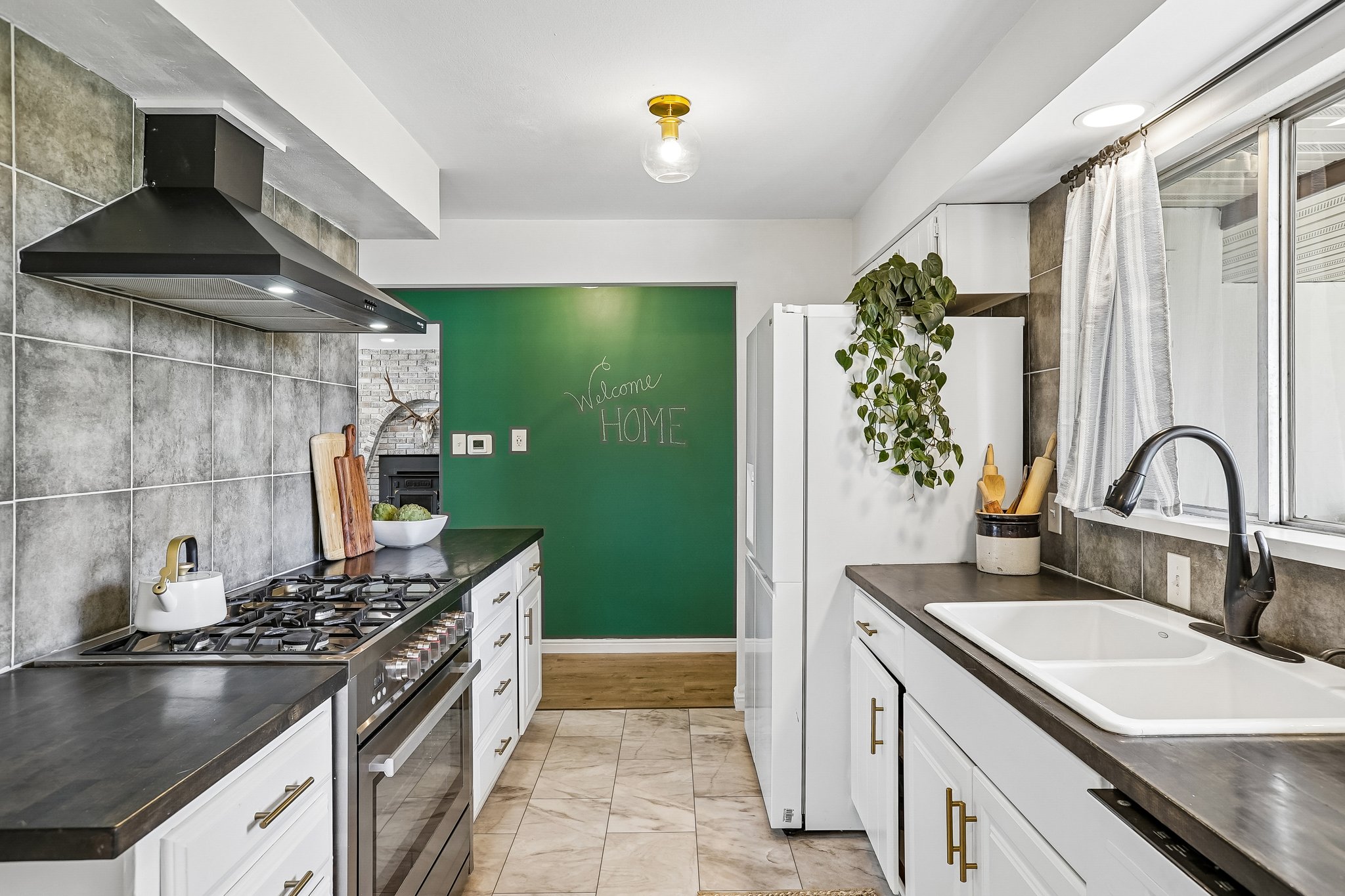 Galley kitchen featuring a gas range, stainless steel oven, white cabinetry with brass hardware, and a double basin sink with a matte black faucet