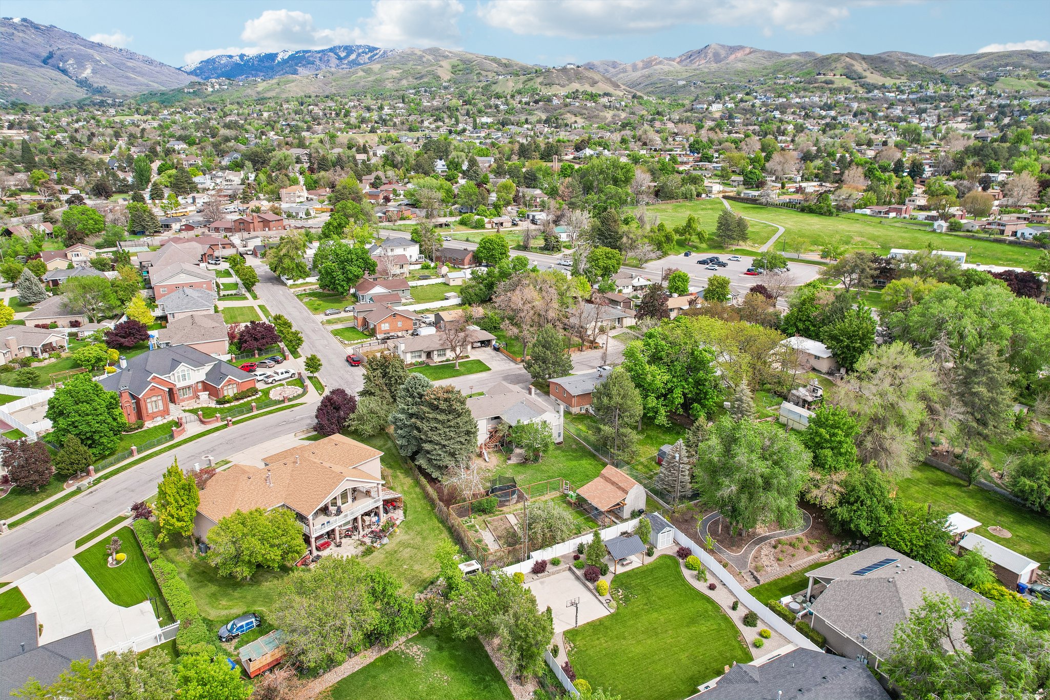 Residential neighborhood with varied architectural styles and mature trees, featuring mountain backdrops, paved streets, and green spaces