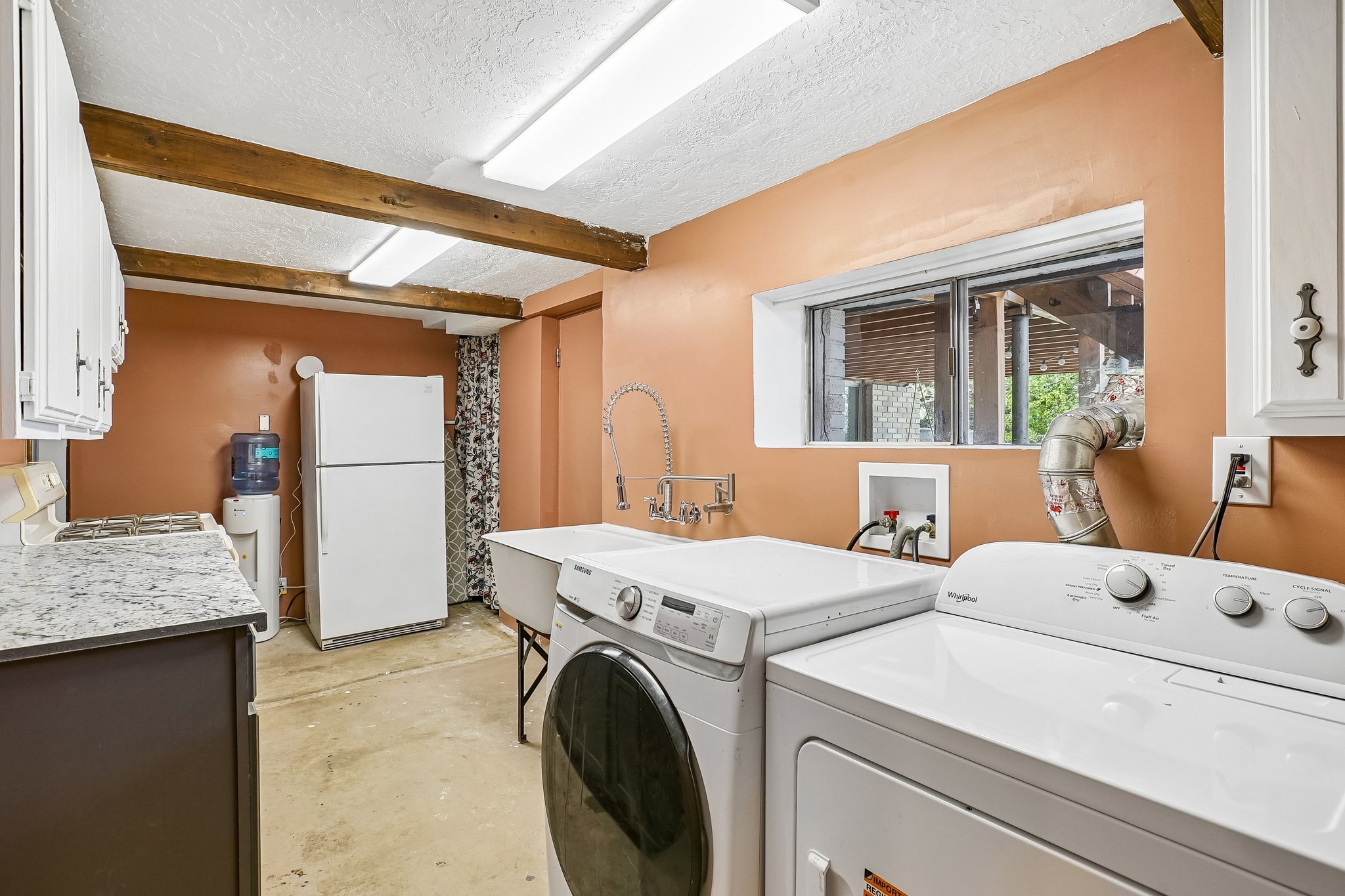 Laundry area featuring a utility sink with a high-arc faucet, a window, and exposed wood beams