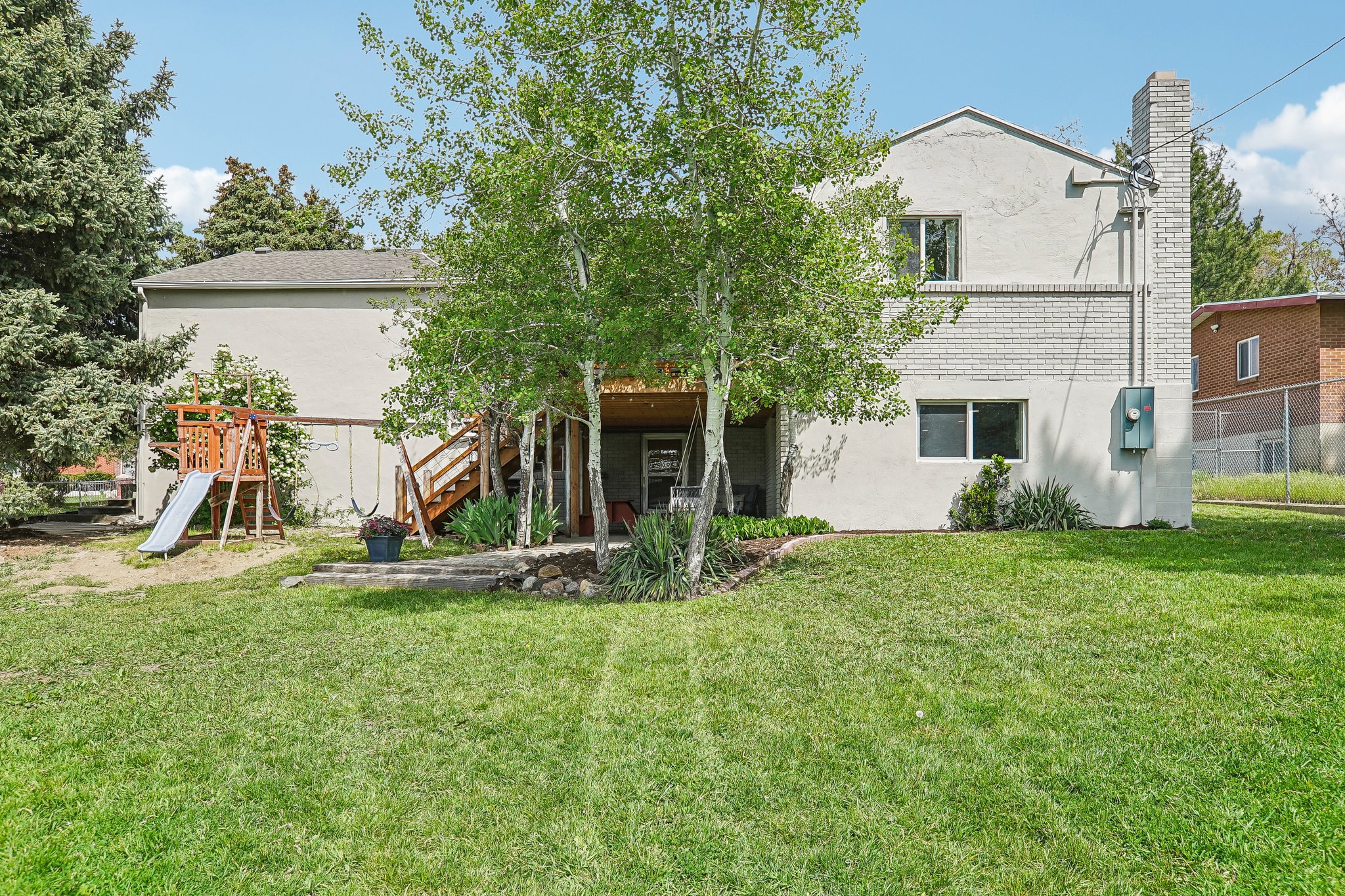 Expansive green lawn with mature trees and a two-story exterior featuring white painted brick and stucco finishes