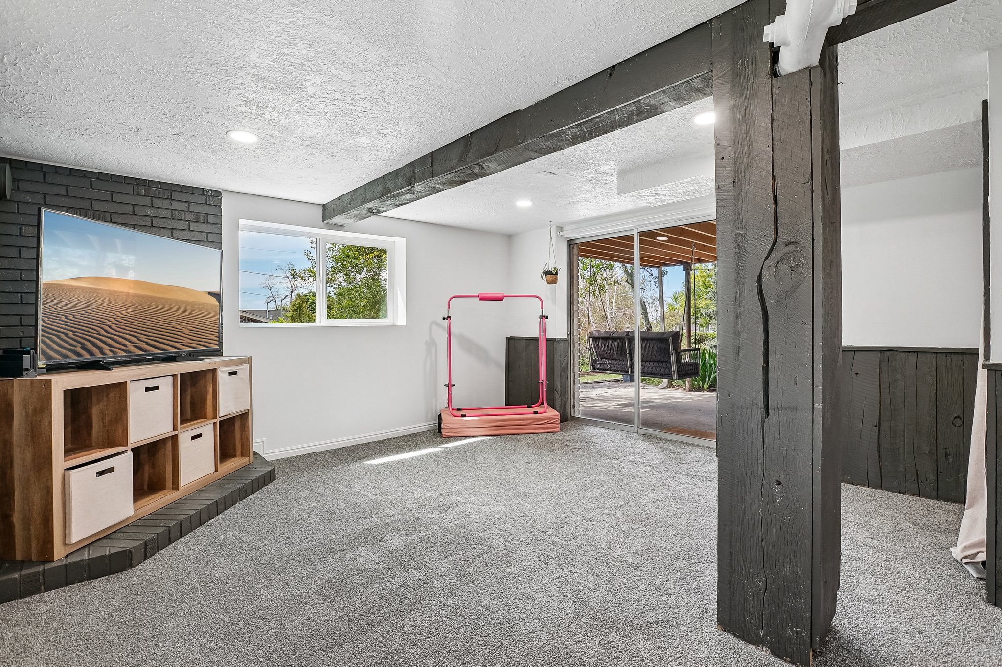 Lower-level room featuring gray carpeting, recessed lighting, and exposed dark wood beams