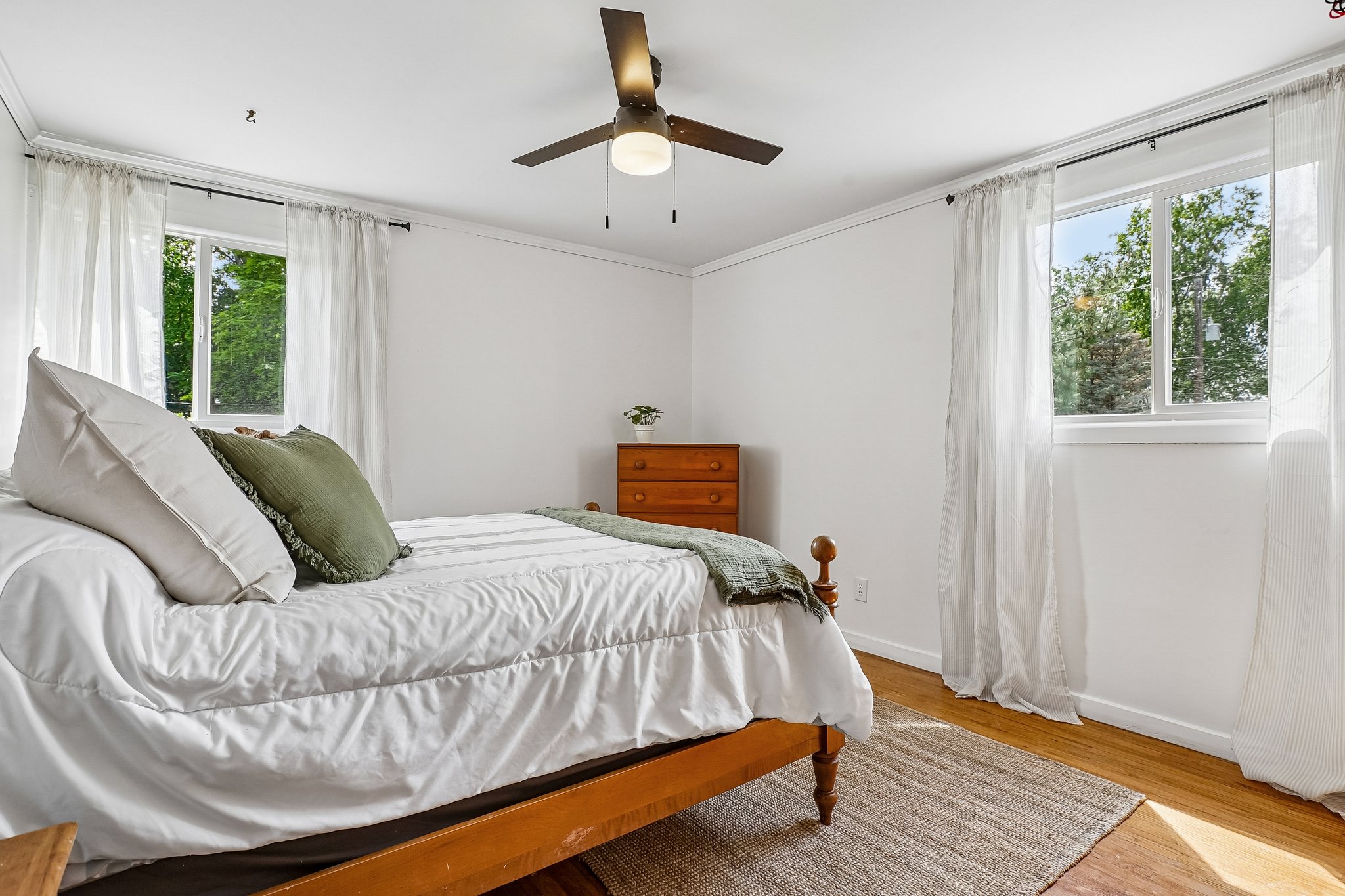 Bright room featuring two windows, wood-finish flooring, a ceiling fan with integrated lighting, and white baseboards