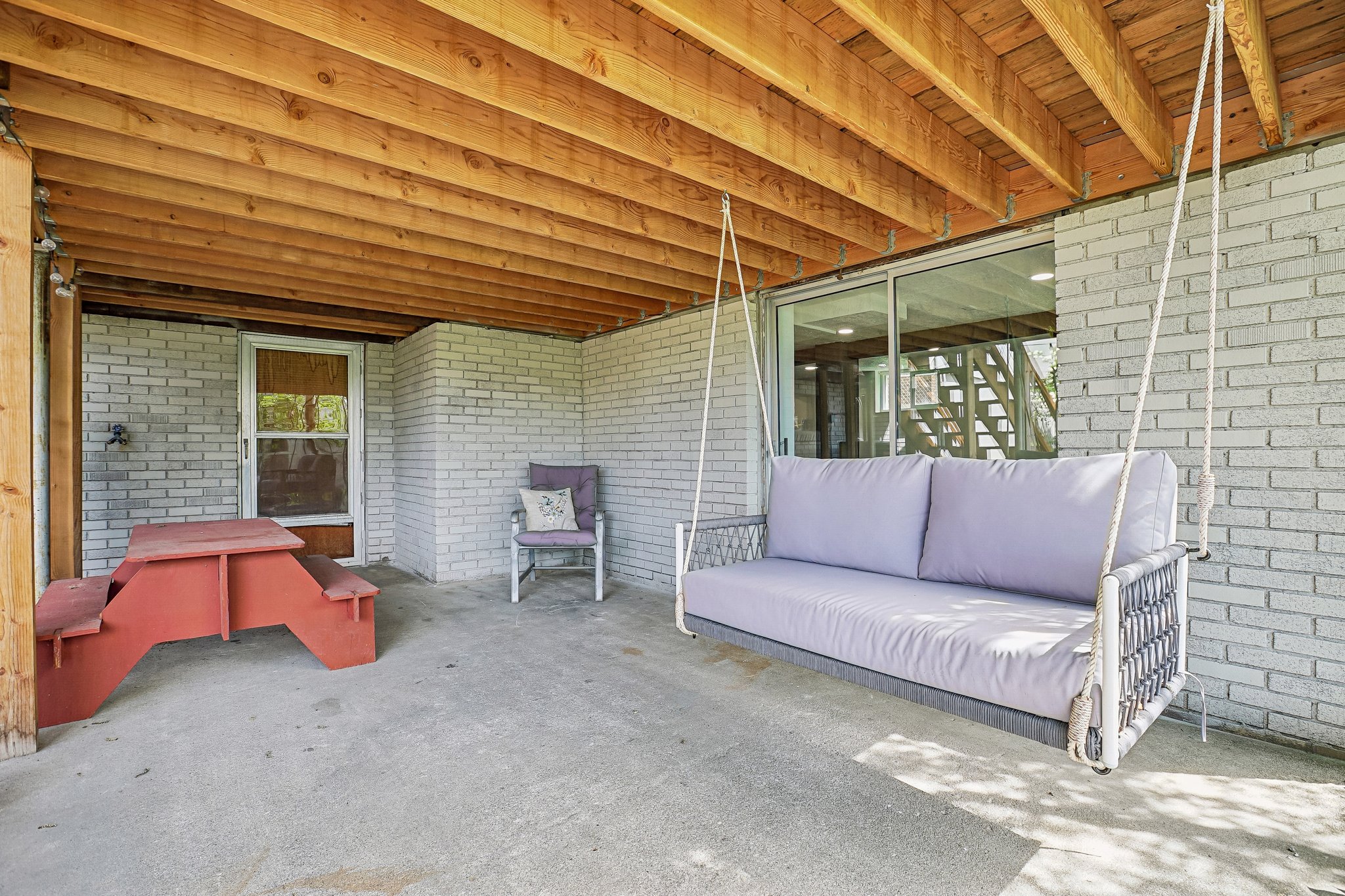 Covered patio space featuring an exposed wood ceiling, light-colored brick walls, concrete flooring, and a glass sliding door