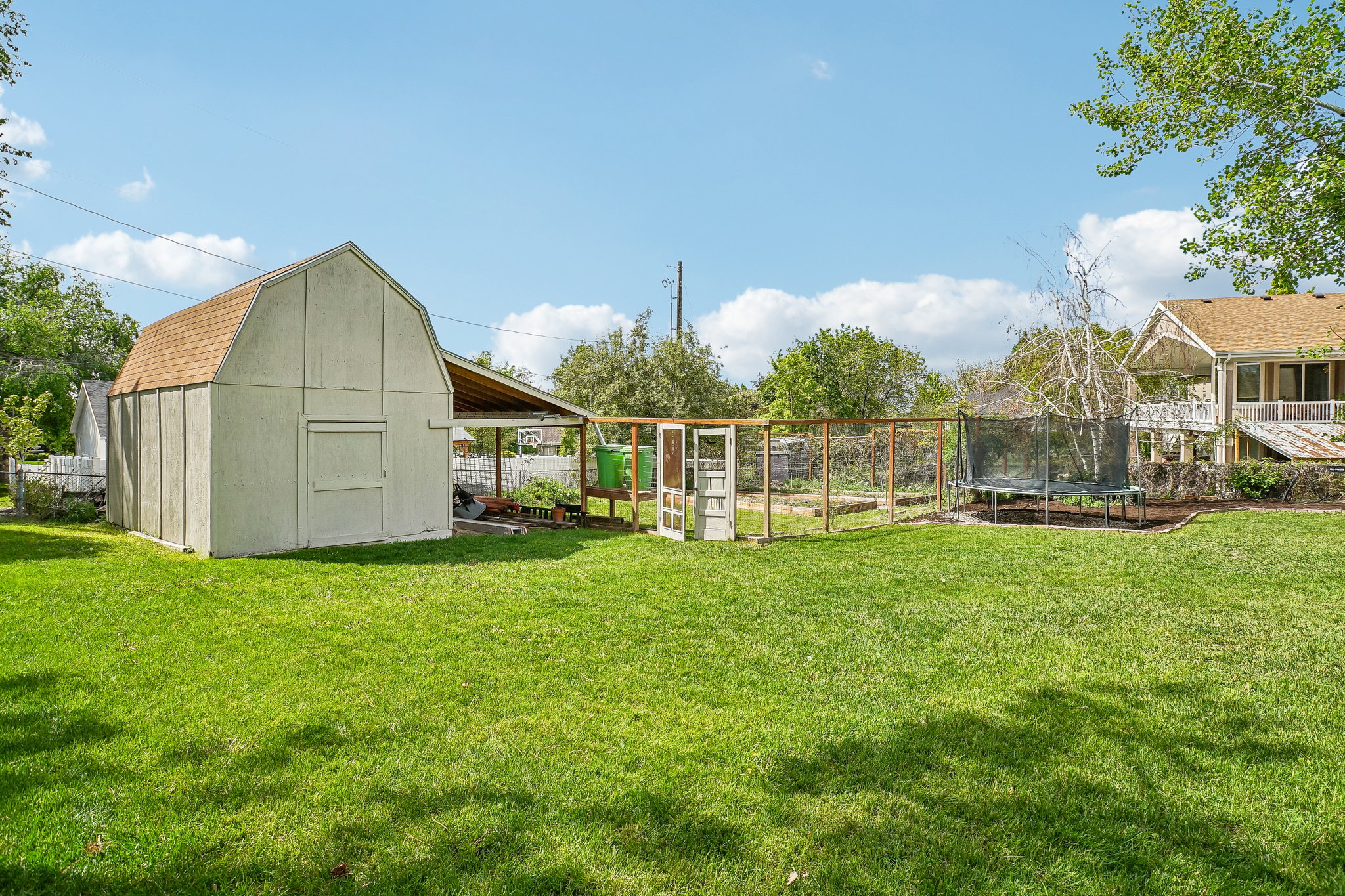Expansive rear yard featuring a large detached barn-style shed with an attached covered area, a fenced garden plot, and a multi-level deck on the main residence