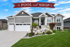 Modern ranch-style home featuring gray siding, stone accents, a three-car garage, manicured front lawn, and a welcoming covered entry