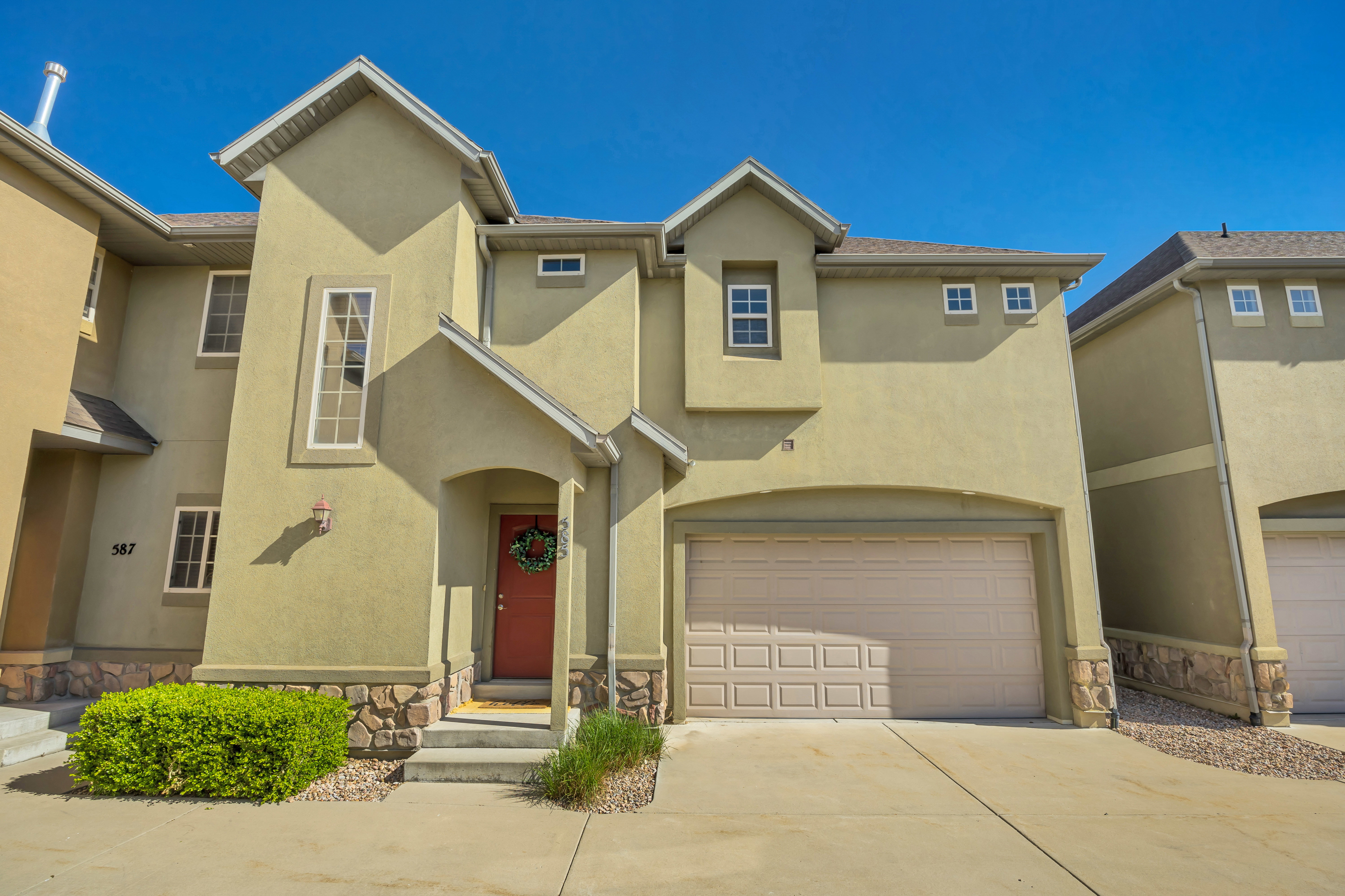 Stucco exterior with stone accents, a concrete driveway, an attached garage, a covered entry, and a red front door