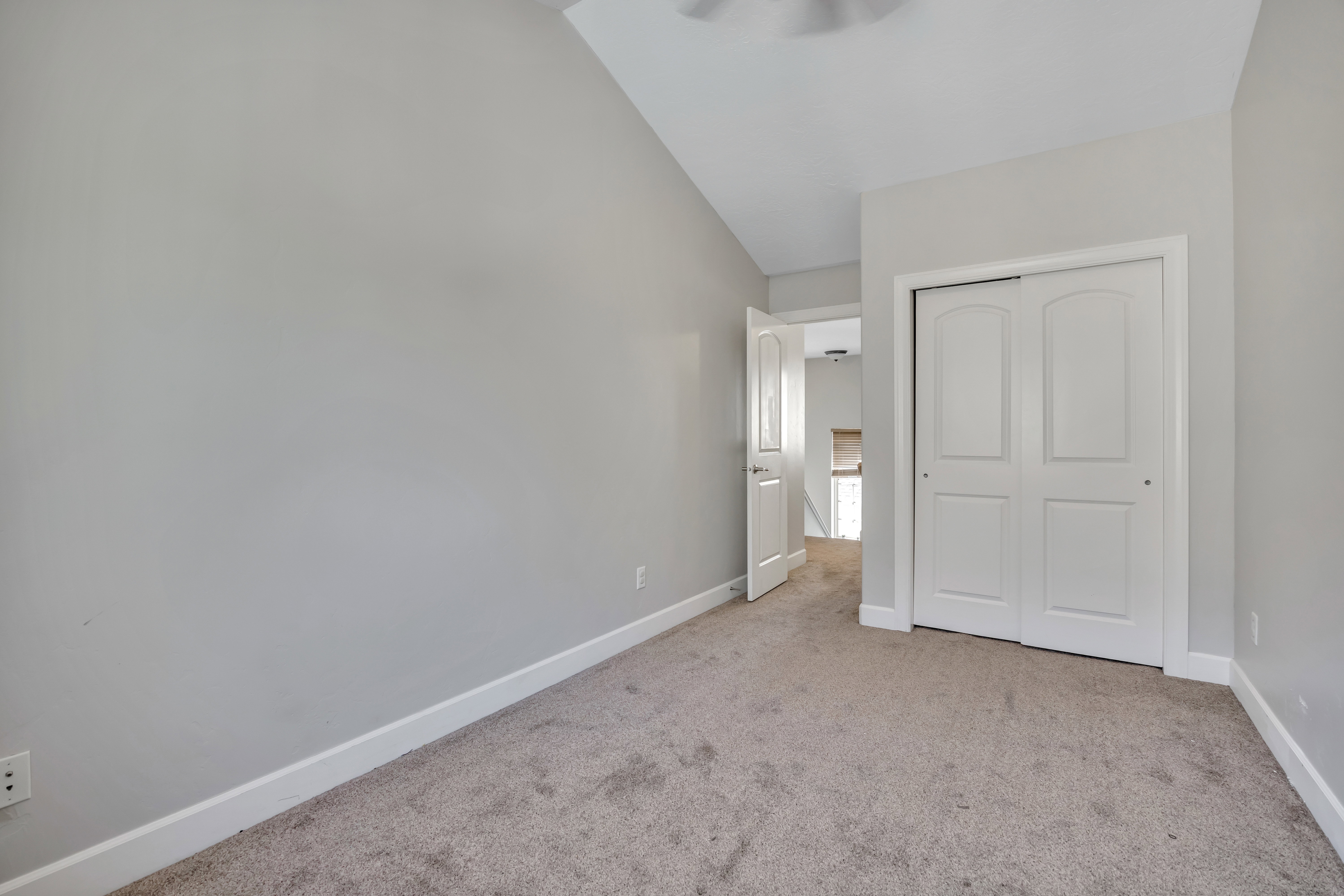 Carpeted room featuring light gray walls, white baseboards, and a white bi-fold closet door