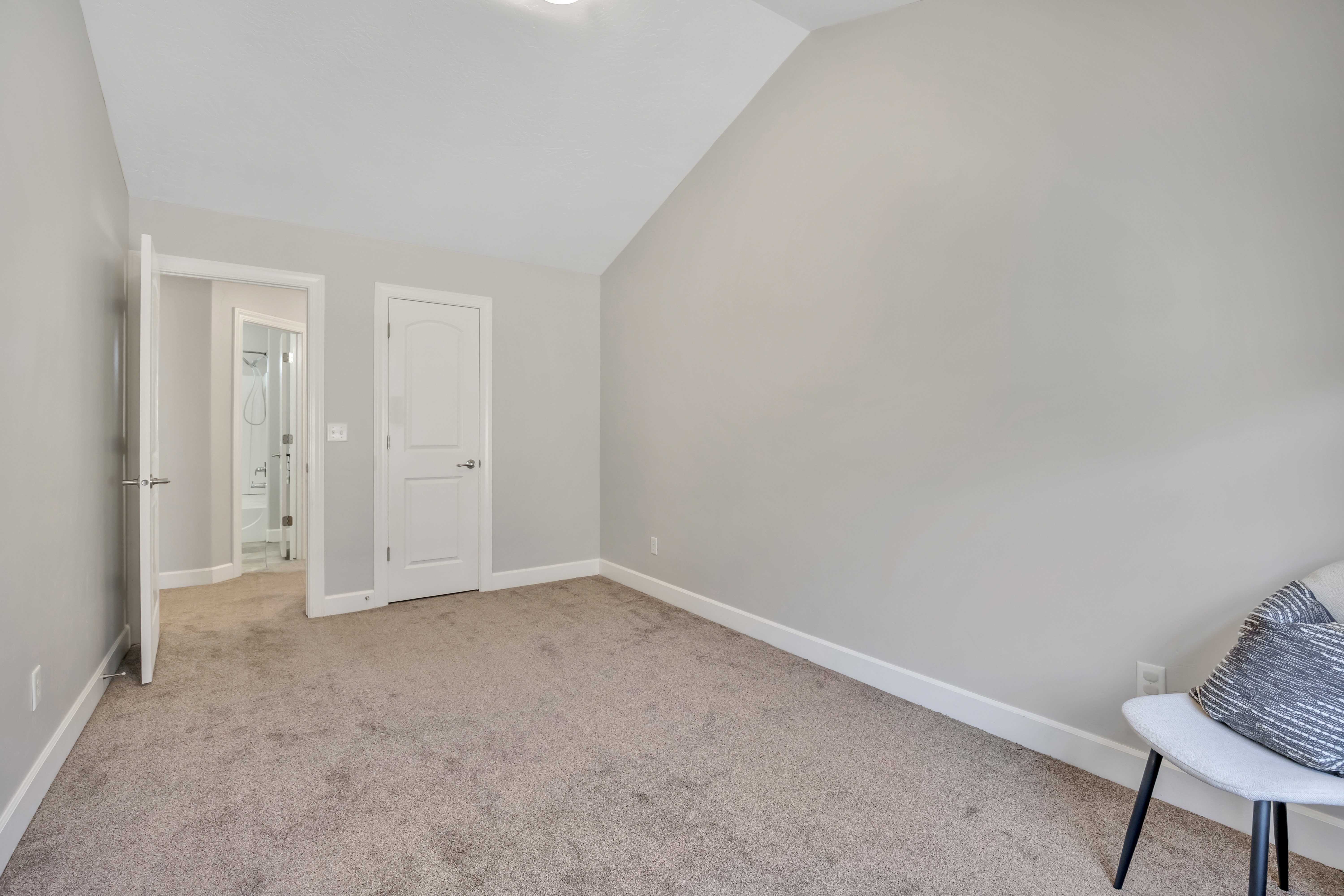 Carpeted room featuring a vaulted ceiling, neutral wall paint, white trim, and a paneled interior door with brushed nickel hardware