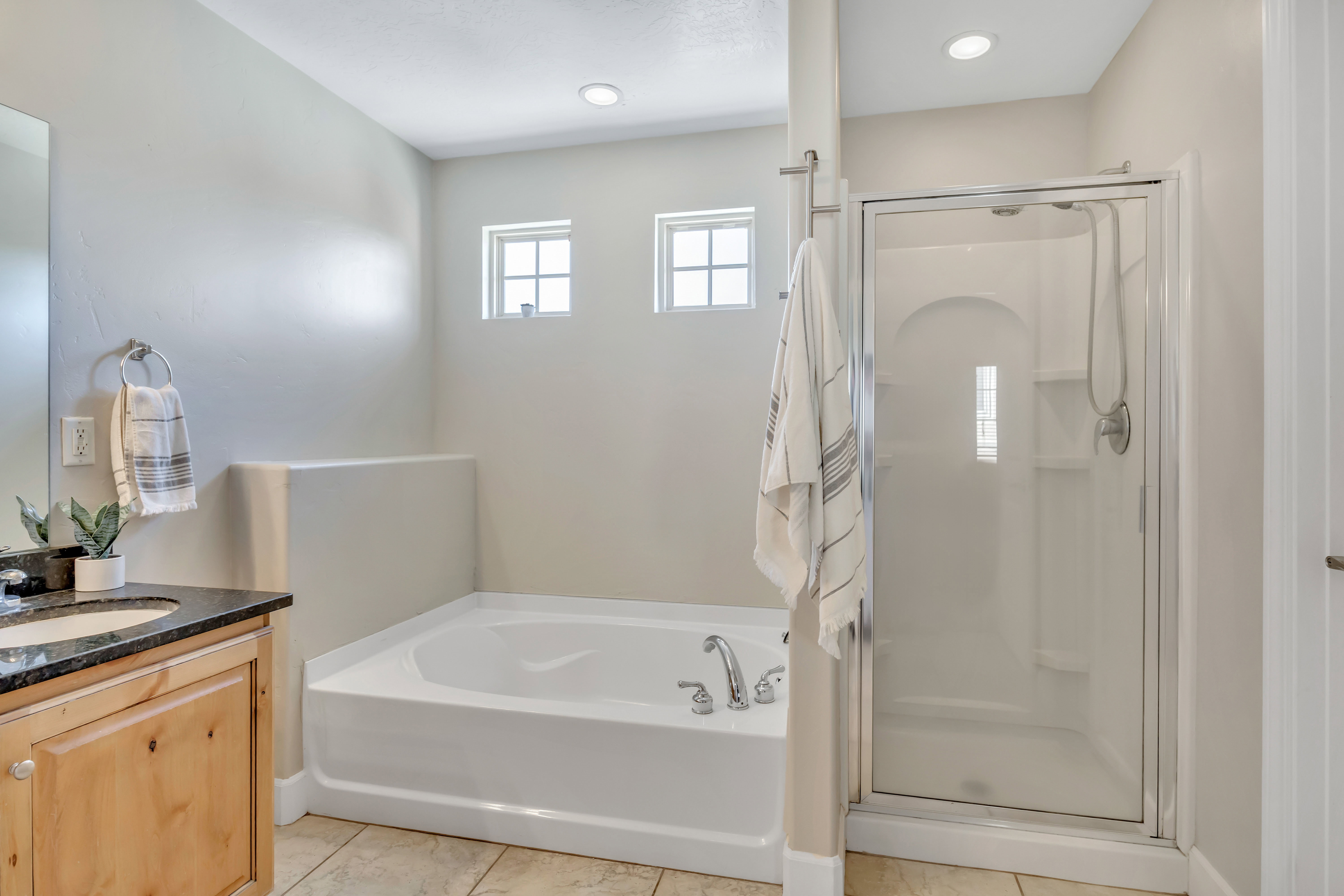 Bathroom featuring a built-in soaking tub, glass-enclosed shower, light wood-finish vanity with a dark countertop, and recessed lighting