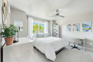 Bedroom featuring carpet flooring, a multi-pane window with white blinds and drapes, a ceiling fan, and a built-in shelving unit