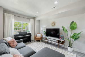 Living area featuring wood-finish flooring, recessed lighting, and a large window with white curtain panels