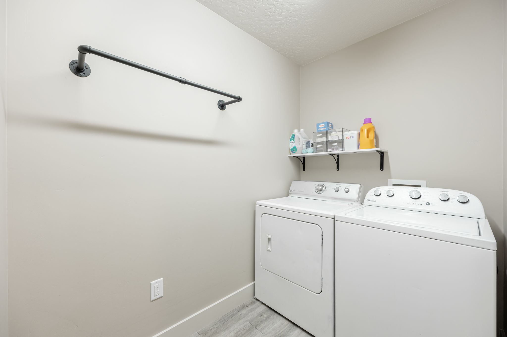 Dedicated laundry area featuring a wall-mounted drying rod, floating shelf, and wood-finish flooring