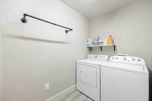 Dedicated laundry area featuring a wall-mounted drying rod, floating shelf, and wood-finish flooring