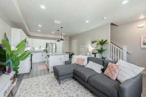 Open-concept living area featuring wood-finish flooring, recessed lighting, and a white staircase with a prominent newel post