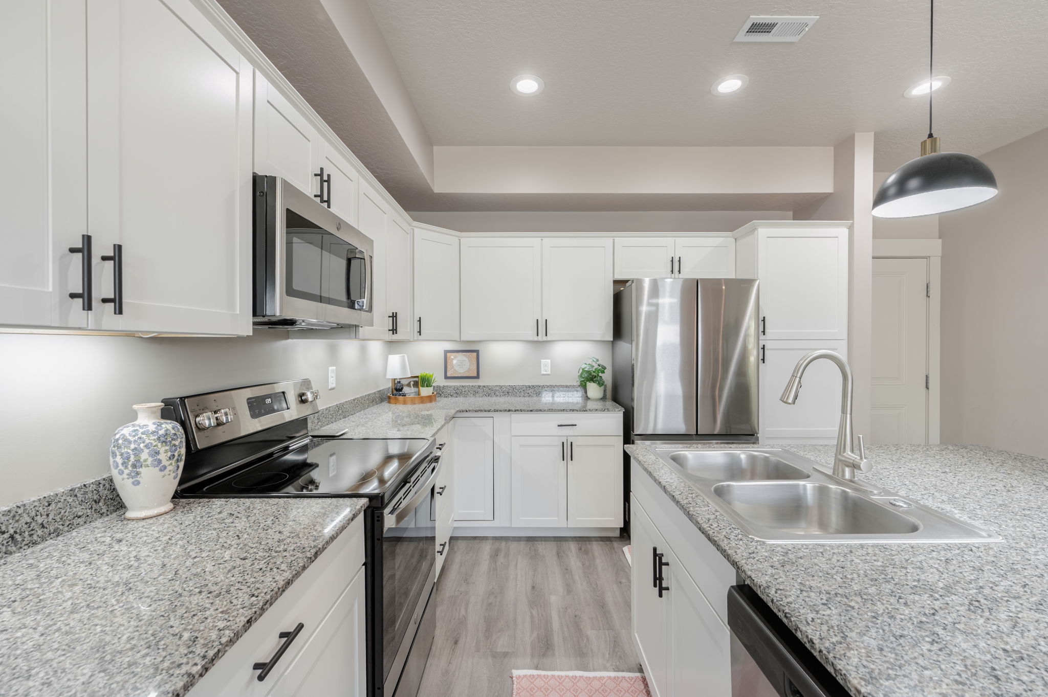 Bright kitchen featuring white shaker cabinetry, stainless steel appliances, speckled stone countertops, and wood-finish flooring
