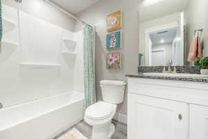 Bathroom featuring a white bathtub and shower surround, a toilet, and a vanity with a dark speckled countertop