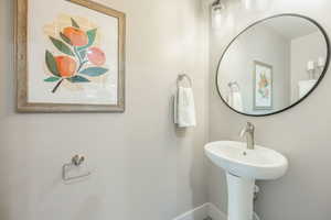 Pedestal sink with a brushed nickel faucet, complemented by a large oval mirror with a black frame and a three-light vanity fixture