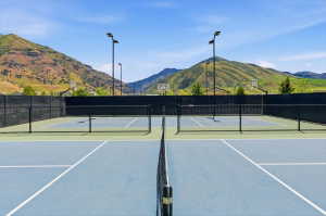 Dual tennis courts with blue and green surfacing, black chain-link fencing, and overhead lighting fixtures