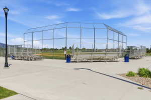 Recreational field featuring a chain-link backstop, multiple spectator bleachers, and a paved concrete pathway