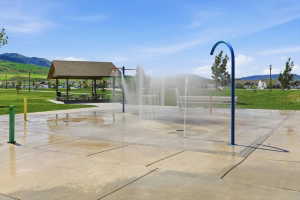 Splash pad with multiple water features, concrete surfacing, and a nearby covered picnic area