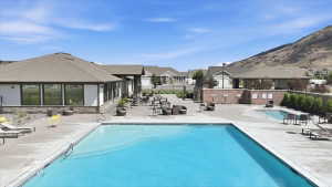 Outdoor swimming pool with a secondary wading pool, surrounding concrete deck, and patio area featuring a modern building with large windows