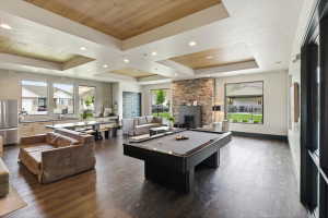 Open-concept common area featuring wood-finish flooring, a stone accent wall with an electric fireplace, a pool table, and recessed ceiling lighting