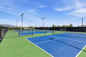 Multiple courts with blue and green surfacing, featuring black chain-link fencing and tall light posts