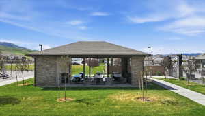 Stone-clad pavilion featuring a shingle roof, multiple picnic tables, and built-in grills