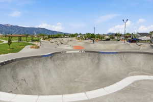 Concrete skate park featuring multiple bowls and ramps, surrounded by green spaces and distant mountains