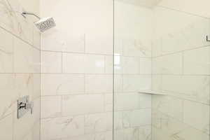 Tiled shower featuring a rectangular rainfall showerhead, chrome fixtures, a clear glass enclosure, and an integrated corner shelf