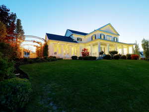 Expansive front lawn with manicured landscaping, leading to a two-story residence featuring a broad wrap-around porch with white columns