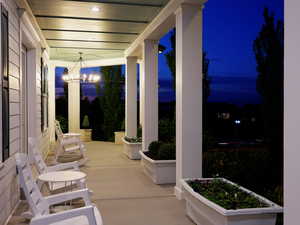 Expansive covered front porch featuring multiple columns, a sophisticated chandelier, recessed lighting, and integrated planter boxes