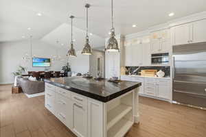 Spacious kitchen featuring a large central island with a dark stone countertop, white cabinetry with chrome hardware, and light wood-finish flooring