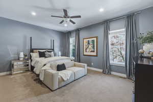 Spacious bedroom featuring light gray walls, plush carpeting, a ceiling fan with integrated lighting, recessed lighting fixtures, and two large windows with full-length drapery rods