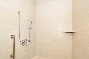 Tiled shower enclosure featuring a handheld showerhead, wall-mounted faucet controls, an integrated corner shelf, and a vertical grab bar