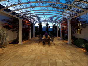 Expansive patio featuring light-toned paver flooring and an arched pergola with integrated lighting
