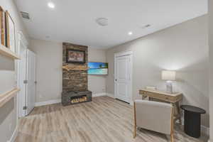 Room featuring wood-finish flooring, a stone-clad fireplace with a wood mantle, recessed lighting, and built-in shelving