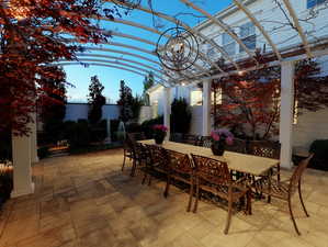 Expansive paver patio with a white pergola, overhead chandelier, and climbing vines