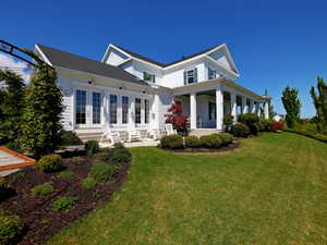 White siding exterior with multiple French doors, an expansive covered porch with white columns, and a large green lawn with mature landscaping