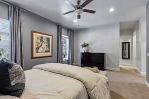 Spacious bedroom featuring neutral carpeting, a ceiling fan with integrated lighting, recessed overhead lighting, and two windows with blinds and drapes