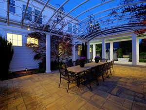 Patio area featuring an arched pergola with integrated lighting, a paver stone surface, perimeter landscaping, and a white architectural facade