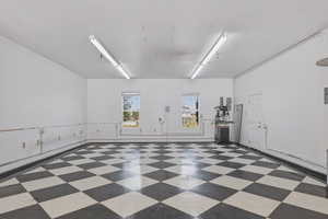 Spacious interior featuring a black and white checkerboard floor, dual windows providing natural illumination, multiple fluorescent overhead light fixtures, and a side access door